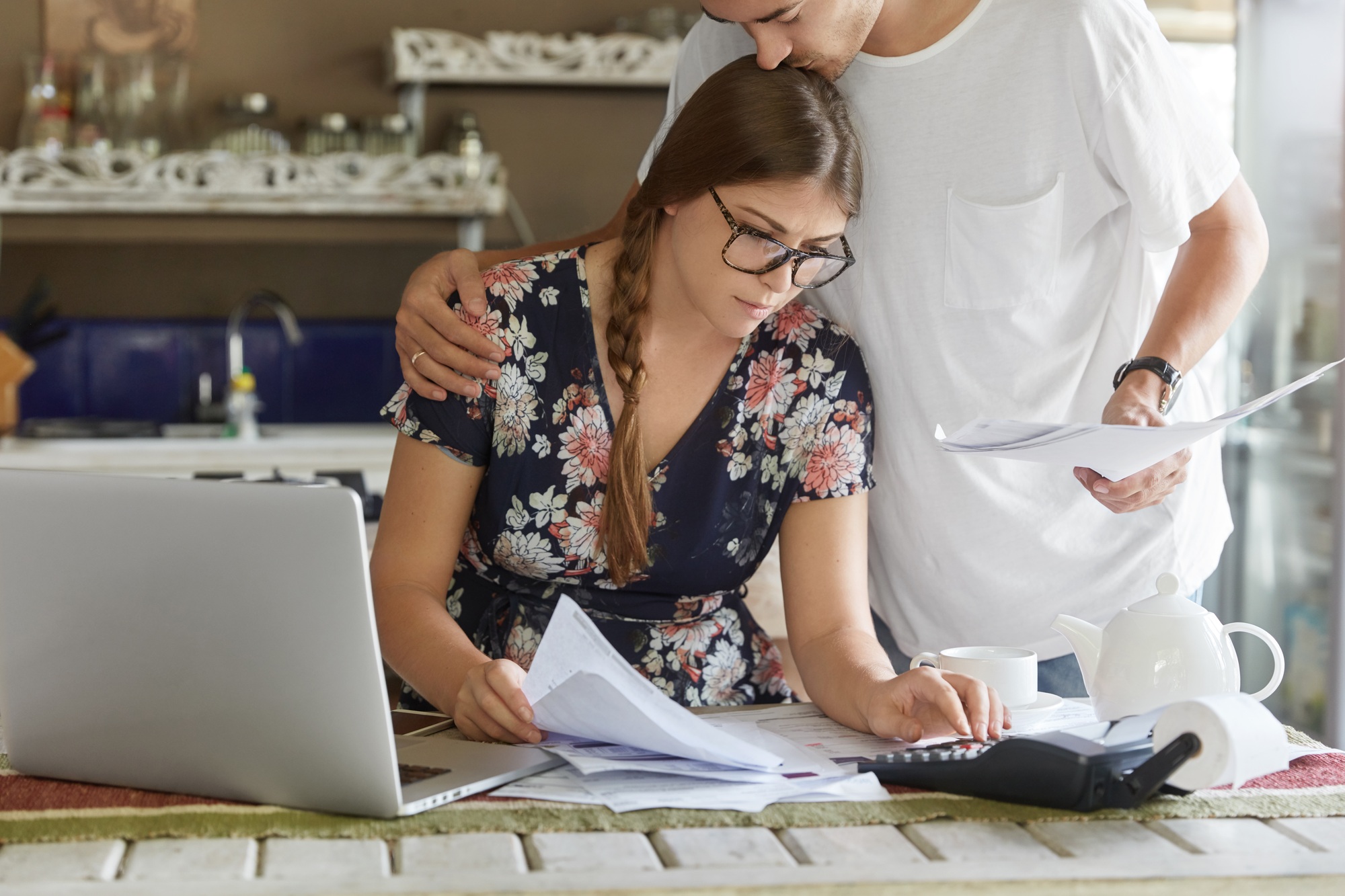 Young family couple consider mortgage loan offer, calculate interest on debt, pose against kitchen i